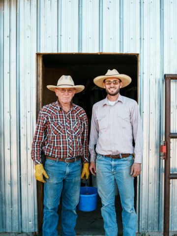Two farmers wearing straw hats stand in a doorway.
